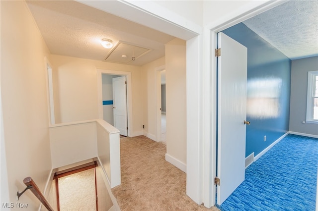 hall with a textured ceiling and light colored carpet