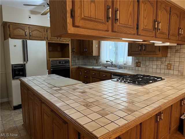 kitchen featuring backsplash, oven, white refrigerator with ice dispenser, ceiling fan, and tile counters