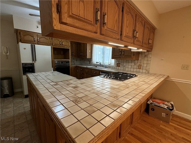 kitchen with tile countertops, tasteful backsplash, wood-type flooring, stainless steel gas stovetop, and sink