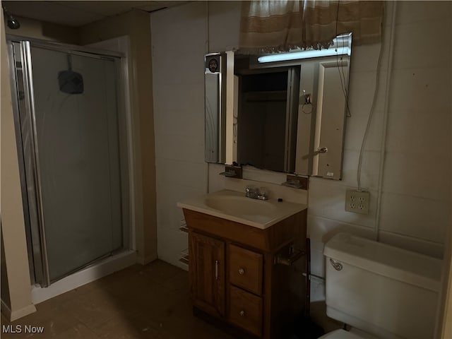 bathroom featuring a shower with shower door, toilet, vanity, and tile walls