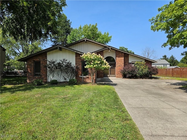 mid-century home featuring brick siding, concrete driveway, a front lawn, and fence