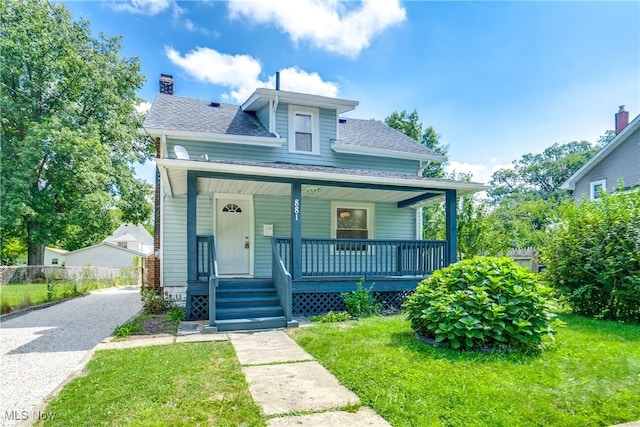 bungalow-style house featuring covered porch, driveway, roof with shingles, a chimney, and a front yard