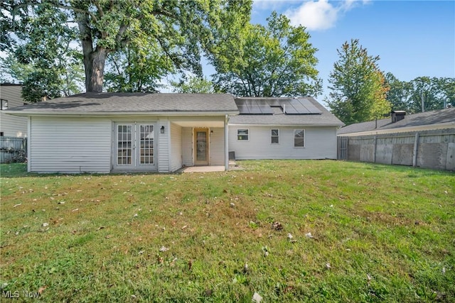 rear view of house featuring solar panels, fence private yard, and a lawn