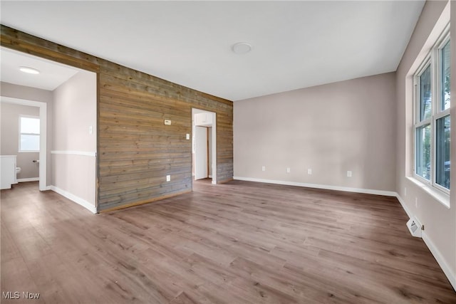 unfurnished room featuring an accent wall, wood finished floors, baseboards, and wood walls