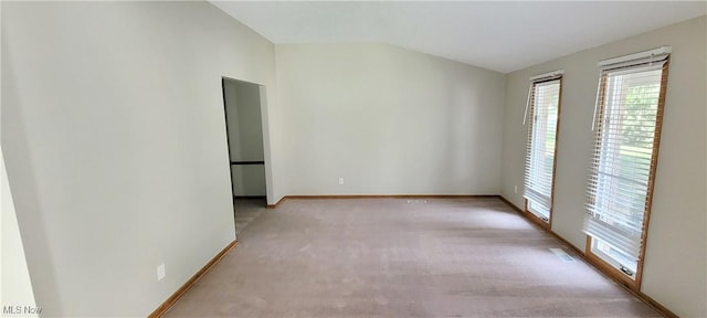 empty room featuring vaulted ceiling, light carpet, visible vents, and baseboards