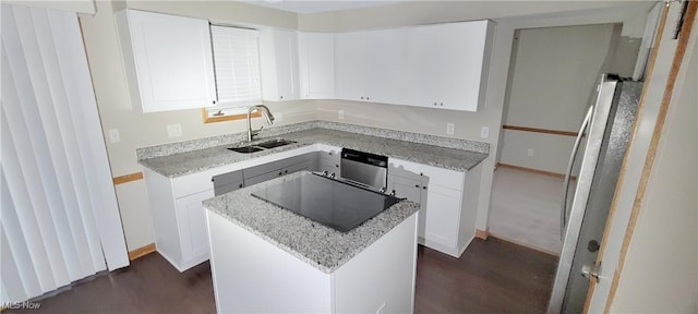 kitchen with appliances with stainless steel finishes, white cabinetry, a sink, a kitchen island, and light stone countertops