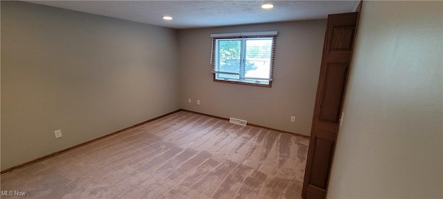 empty room with light colored carpet, visible vents, a textured ceiling, and baseboards