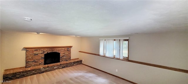 unfurnished living room with a brick fireplace, wood finished floors, and baseboards