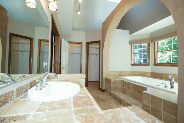 bathroom with sink and tiled bath