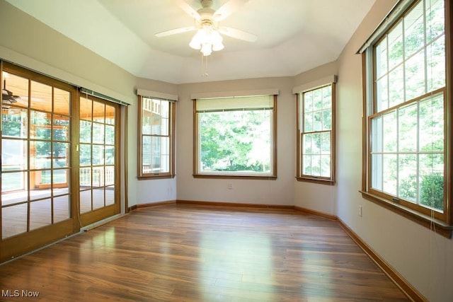 unfurnished sunroom with ceiling fan, a wealth of natural light, and a tray ceiling