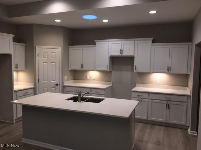 kitchen with a kitchen island with sink, sink, white cabinets, and dark wood-type flooring