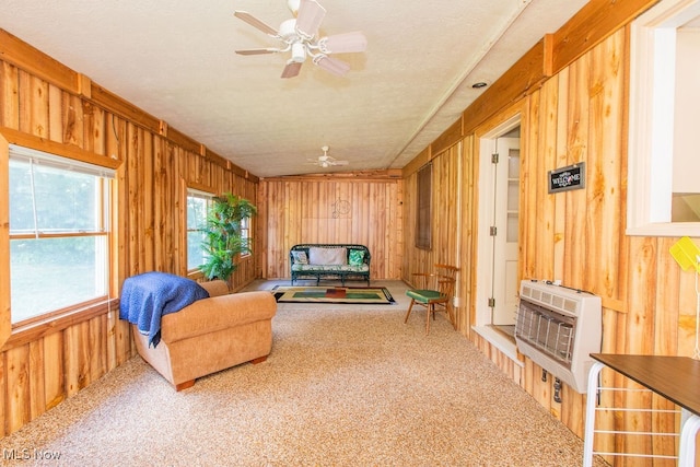 living area with heating unit, carpet floors, wood walls, ceiling fan, and a textured ceiling