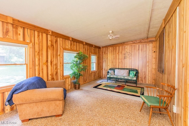 living area with lofted ceiling, wood walls, ceiling fan, and carpet