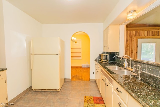 kitchen featuring backsplash, sink, white refrigerator, dark stone counters, and light tile patterned flooring