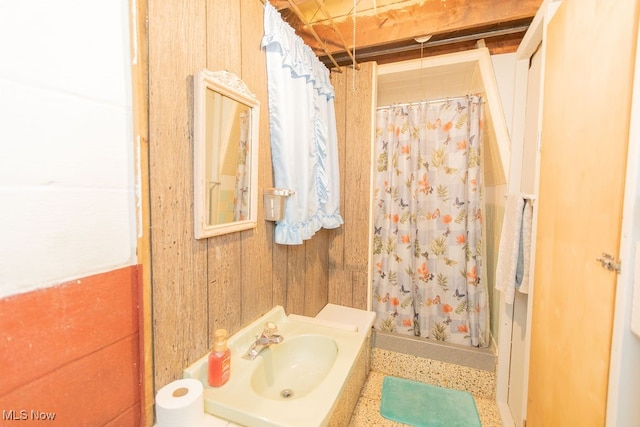 bathroom with curtained shower, wood walls, and sink