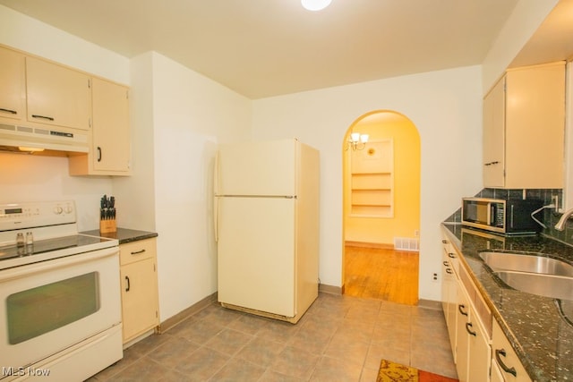 kitchen featuring dark stone counters, white appliances, tasteful backsplash, light tile patterned floors, and sink