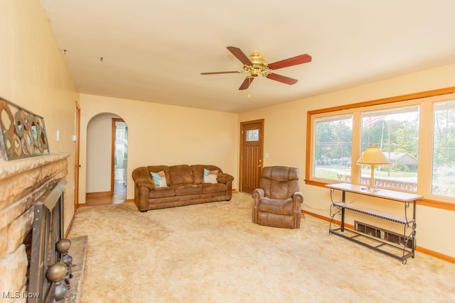 carpeted living room with ceiling fan and a stone fireplace