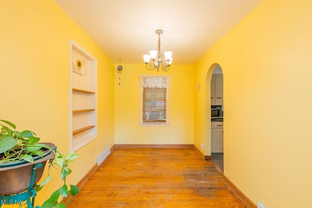 hallway with built in shelves, an inviting chandelier, and light hardwood / wood-style floors