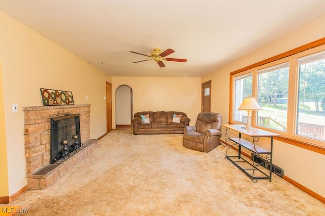 living room featuring light carpet, ceiling fan, and a stone fireplace