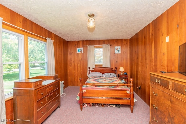 carpeted bedroom with a textured ceiling, wooden walls, and multiple windows