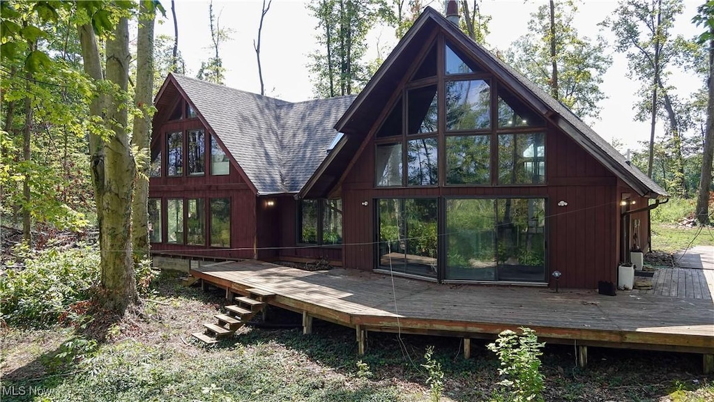 rear view of property featuring roof with shingles, a wooden deck, and a sunroom