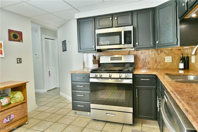 kitchen featuring appliances with stainless steel finishes, a paneled ceiling, light tile patterned floors, decorative backsplash, and sink