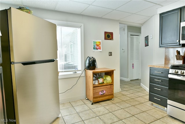 kitchen with appliances with stainless steel finishes, light tile patterned floors, backsplash, and a drop ceiling