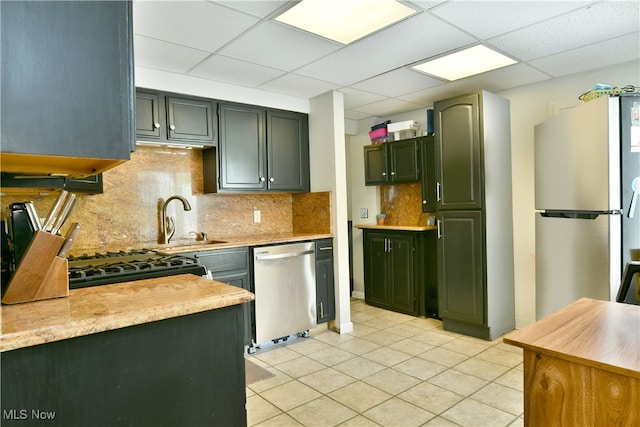 kitchen featuring sink, a drop ceiling, light tile patterned flooring, tasteful backsplash, and appliances with stainless steel finishes