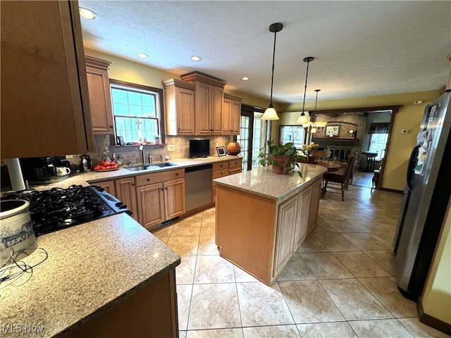 kitchen with hanging light fixtures, a fireplace, appliances with stainless steel finishes, sink, and a kitchen island