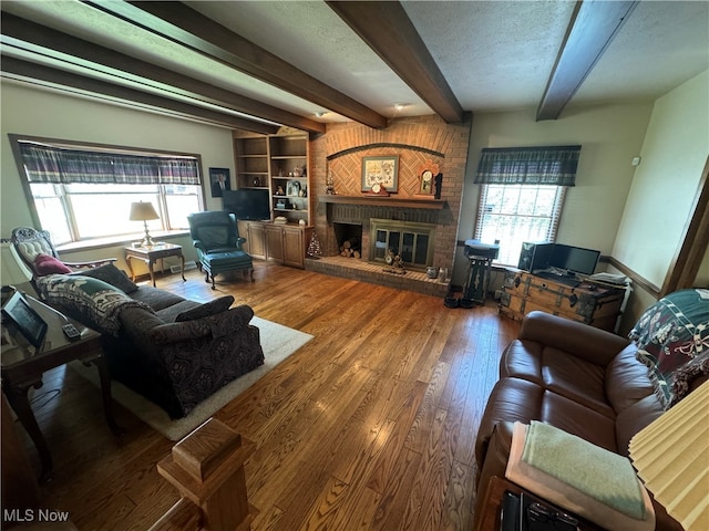 living room featuring a textured ceiling, hardwood / wood-style flooring, a brick fireplace, and beam ceiling