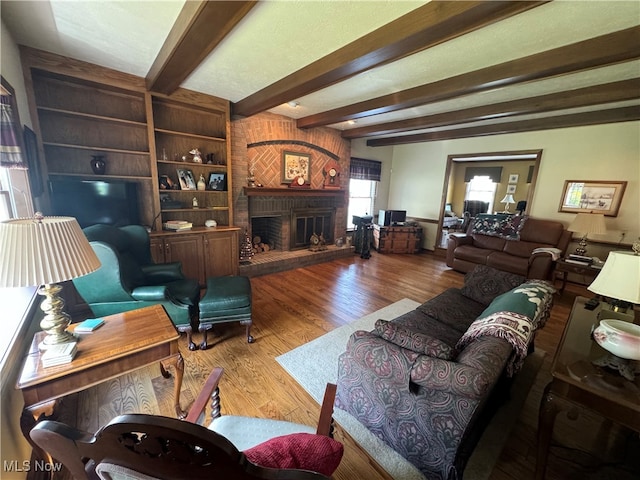 living room featuring beamed ceiling, a brick fireplace, wood-type flooring, and built in shelves