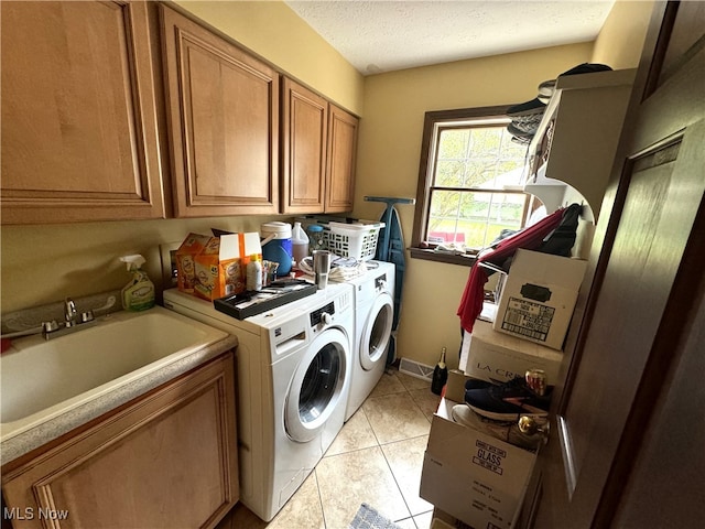 laundry area with a textured ceiling, cabinets, light tile patterned floors, independent washer and dryer, and sink