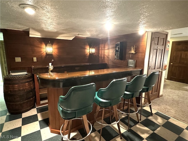 bar featuring a textured ceiling, light carpet, and wooden walls