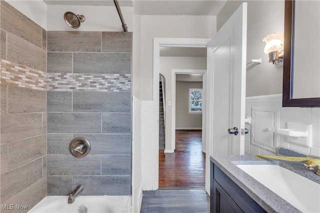 bathroom featuring hardwood / wood-style floors, tiled shower / bath, tile walls, and vanity