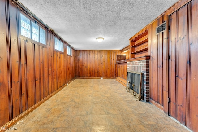 unfurnished living room with wood walls, a textured ceiling, and a brick fireplace