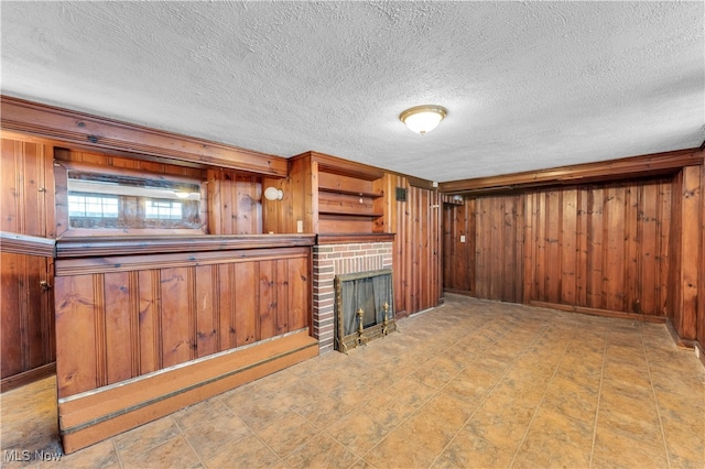 unfurnished living room featuring wood walls, a textured ceiling, and a brick fireplace