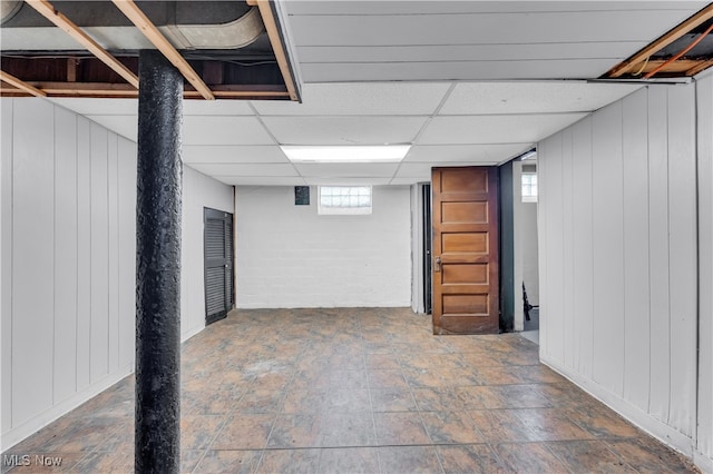 basement with plenty of natural light, a paneled ceiling, and wooden walls