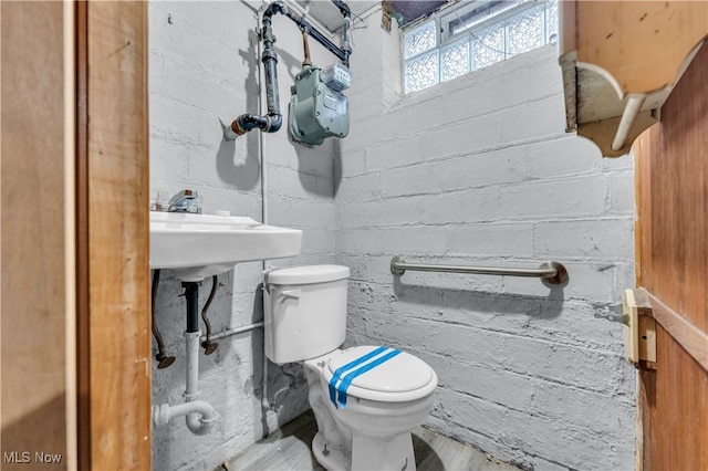 bathroom featuring toilet, hardwood / wood-style flooring, and brick wall