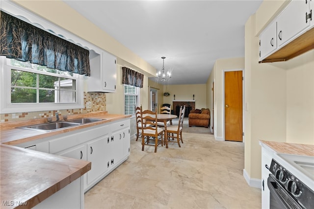 kitchen featuring backsplash, black range oven, sink, a chandelier, and white cabinets