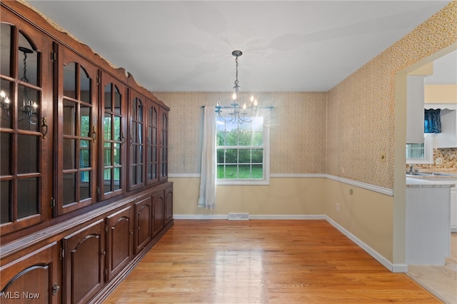 unfurnished dining area with light wood-type flooring and a notable chandelier