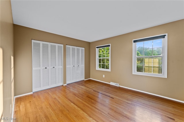 unfurnished bedroom featuring multiple closets and light hardwood / wood-style floors