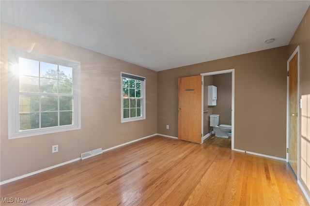 unfurnished bedroom with light wood-type flooring, multiple windows, and ensuite bathroom