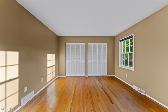 unfurnished bedroom featuring light hardwood / wood-style flooring and multiple closets