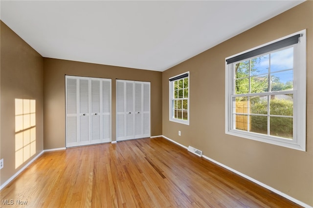 unfurnished bedroom with light hardwood / wood-style flooring and two closets