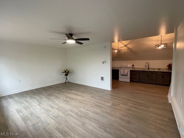 unfurnished living room featuring hardwood / wood-style flooring, sink, vaulted ceiling, and ceiling fan