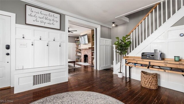 foyer with crown molding, ceiling fan, dark hardwood / wood-style floors, and a brick fireplace