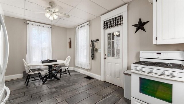 kitchen with gas range gas stove, white cabinets, ceiling fan, and a wealth of natural light