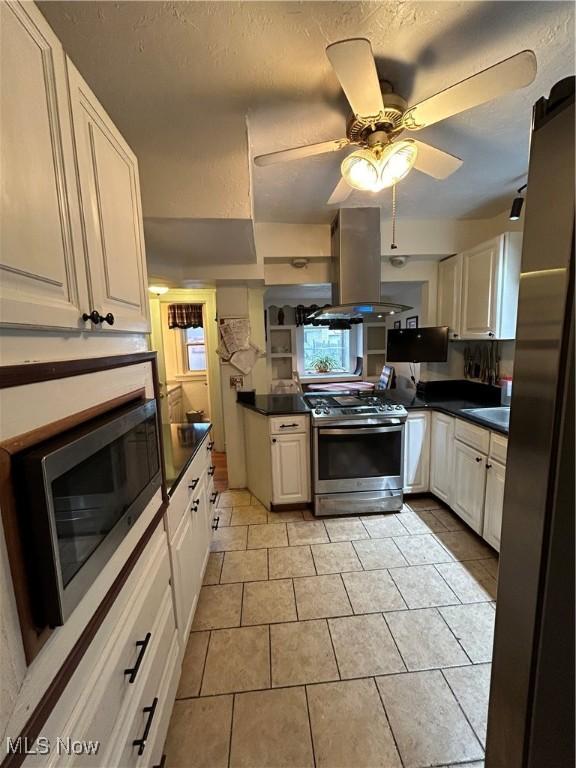 kitchen featuring ceiling fan, stainless steel appliances, island range hood, and a textured ceiling