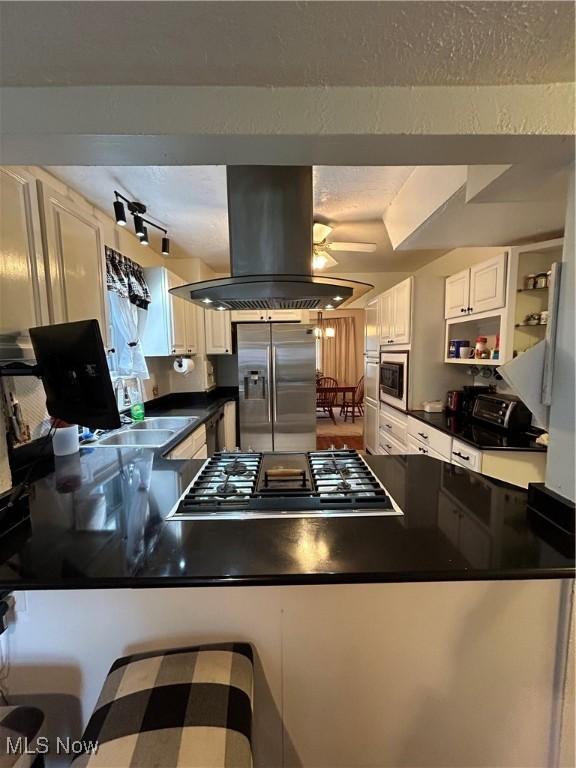 kitchen with appliances with stainless steel finishes, island exhaust hood, kitchen peninsula, ceiling fan, and white cabinets