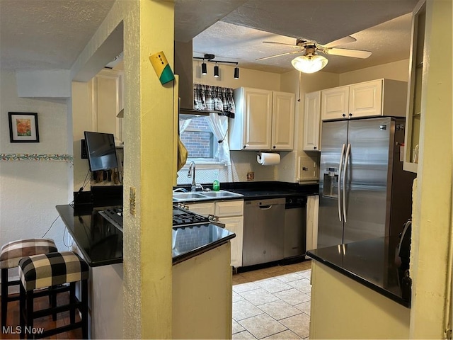 kitchen featuring a textured ceiling, ceiling fan, a sink, appliances with stainless steel finishes, and dark countertops